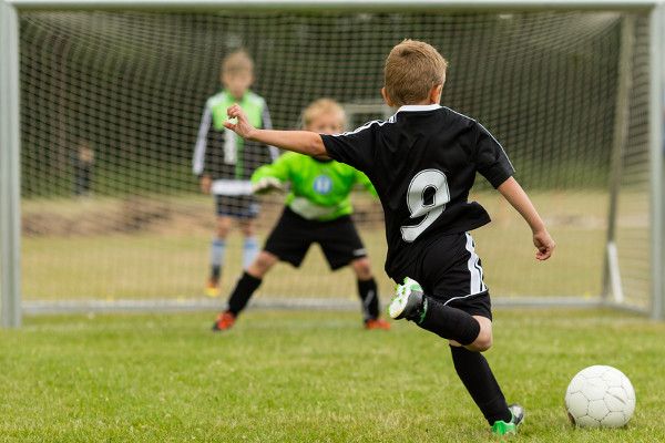 Young goalkeeper wearing gloves catching a ball during training in a small goal